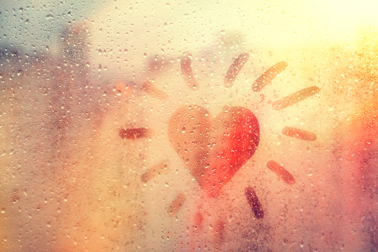 Hand drawn orange shape heart like sun for text on muddy glass wet orange window in city on sunset